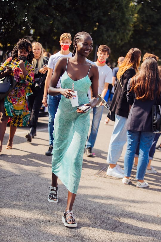 MILAN, ITALY - SEPTEMBER 23: Model Adut Akech wears a green Etro paisley slip dress and white Chanel studded sandals and holds a white Russell x Boss soda cup at the Boss x Russell Athletic show during the Milan Fashion Week - Spring / Summer 2022 on September 23, 2021 in Milan, Italy. (Photo by Melodie Jeng/Getty Images)