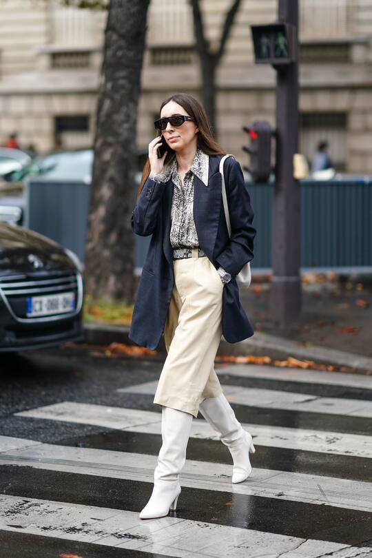 PARIS, FRANCE - OCTOBER 01: A guest wears sunglasses, a grey python pattern shirt, a grey python pattern belt, a beige leather divided skirt, a navy blue Prince of Wales check jacket, white pointy heeled knee-high boots, outside Miu Miu, during Paris Fashion Week - Womenswear Spring Summer 2020, on October 01, 2019 in Paris, France. (Photo by Edward Berthelot/Getty Images)