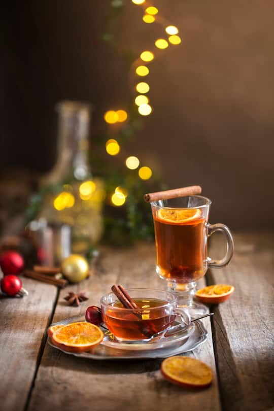 Glasses of cinnamon berry orange hot tea served on rustic moody wooden table top background.