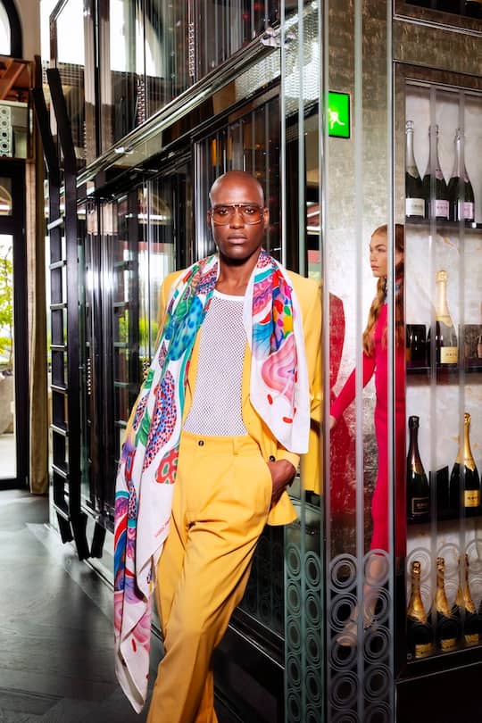 a male model standing leaning on a shelf wearing a colourful outfit
