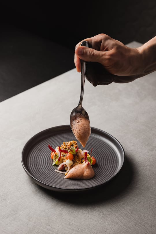 a hand placing food delicately on a black plate