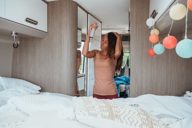 Road trip concept, woman living the van life experience. She sprays her hair at the back of her camper