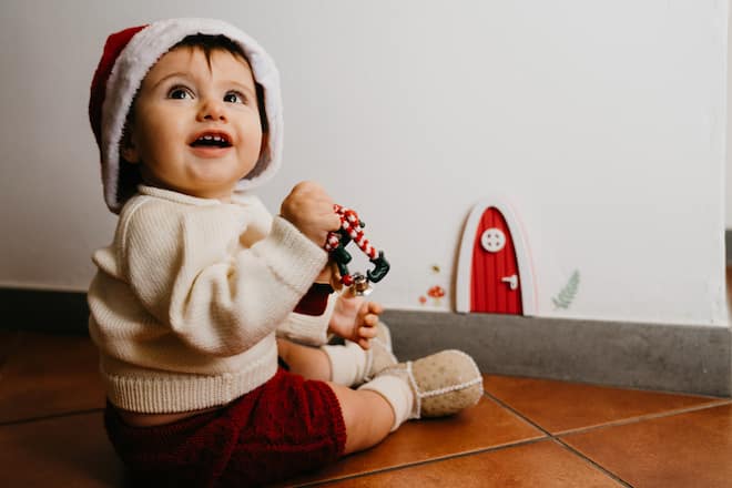 Little kid sitting near a gnomes door. He's wearing a santa hat.