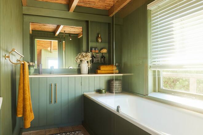 Bathtub and counter in a bathroom with green wood-paneled walls in a holiday home