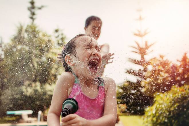 Girl (4-5) in bathing suit sprayed with water hose.