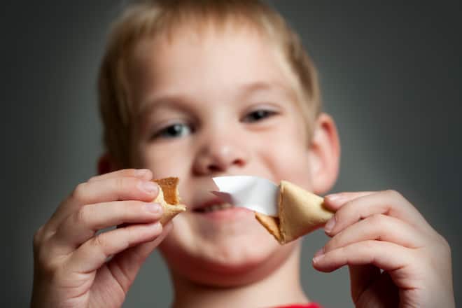 Young boy holds fortune cookie with big smile on his face.
