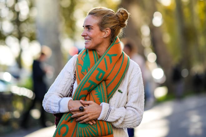 PARIS, FRANCE - OCTOBER 05: Blanca Miro wears an orange and green print pattern wool large scarf, a white braided wool pullover from Lacoste, a black with diamond ring between fingers from Cartier, outside Lacoste, during Paris Fashion Week - Womenswear Spring Summer 2022, on October 05, 2021 in Paris, France. (Photo by Edward Berthelot/Getty Images)