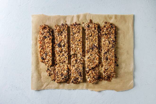 Cutting homemade energy oats granola bars with dried fruits and nuts on baking paper over white texture background. Healthy snack. Flat lay. space. (Photo by: Natasha Breen/REDA&CO/Universal Images Group via Getty Images)