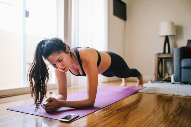 Young woman is doing fitness at her home in Los Angeles, California. She is watching the training on her smartphone for instructions.