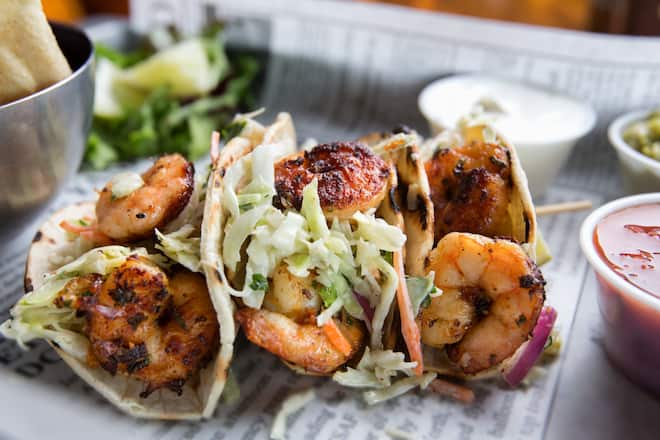 Grilled jumbo shrimp in corn tortilla tacos with cabbage garnish on an old fashioned newspaper wrapper.