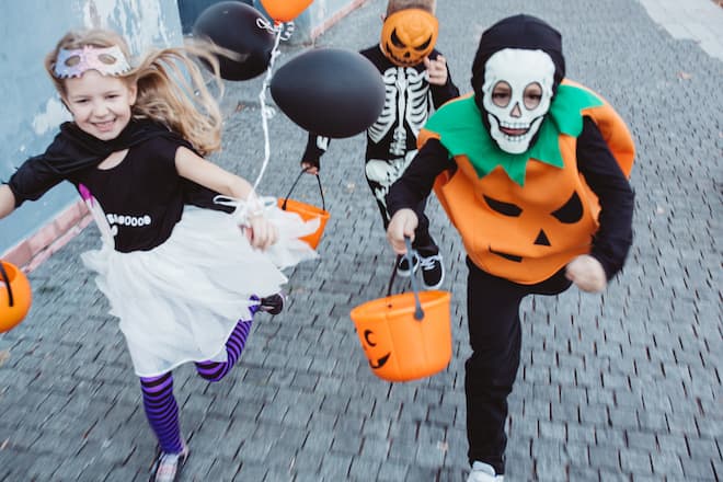 Multi ethnic group of children go for trick or treat, they wear costumes and running trough street to get some sweets.