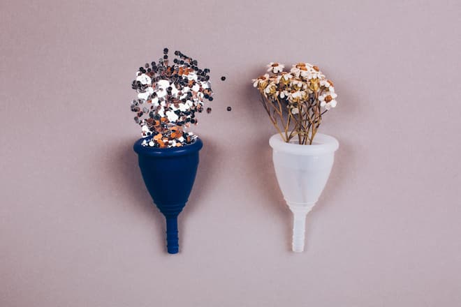 Two menstrual zero waste cups with confetti and chamonile. Alternative reusable product female hygiene. Flat lay style.